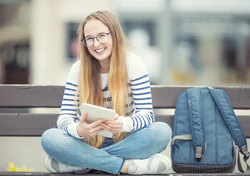 Portrait of a smiling beautiful teenage girl with dental braces. Young schoolgirl with school bag and tablet device.