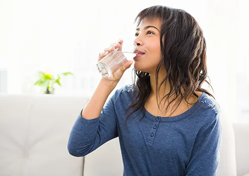 Casual smiling woman drinking some water at home